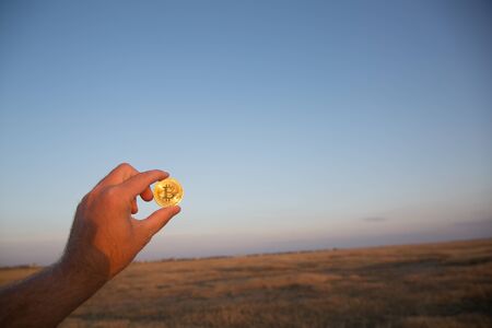 Man holds golden bitcoin at sunset