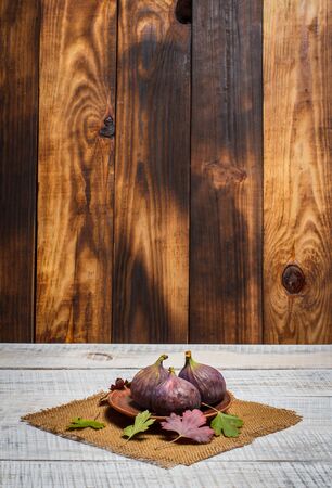 Three ripe figs on a white wooden surface with a brown backgroundの写真素材
