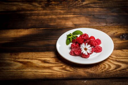 Ripe raspberries and flower on a wooden surfaceの写真素材