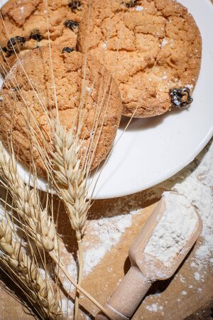 Oatmeal cakes with raisins, flour and spikelets of wheat on a wooden brown surfaceの写真素材
