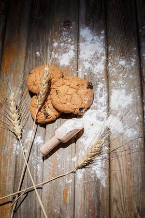Oatmeal cakes with raisins, flour and spikelets of wheat on a wooden brown surfaceの写真素材