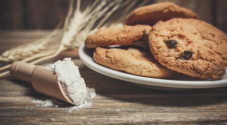Oatmeal cakes with raisins, flour and spikelets of wheat on a wooden brown surfaceの写真素材