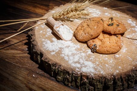 Oatmeal cakes with raisins, flour and spikelets of wheat on a wooden brown surfaceの写真素材