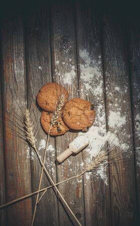 Oatmeal cakes with raisins, flour and spikelets of wheat on a wooden brown surfaceの写真素材