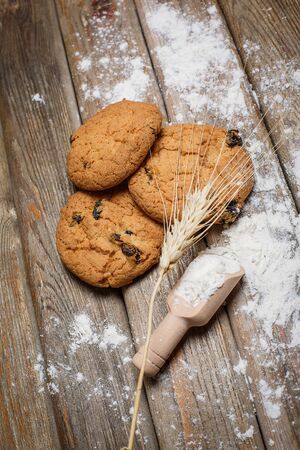 Oatmeal cakes with raisins, flour and spikelets of wheat on a wooden brown surfaceの写真素材
