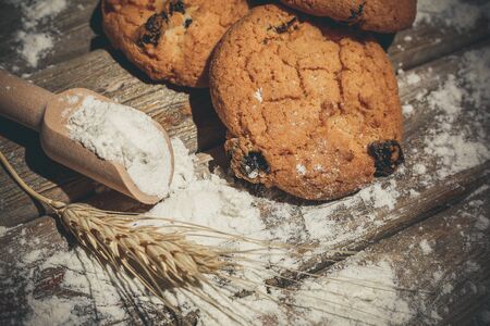 Oatmeal cakes with raisins, flour and spikelets of wheat on a wooden brown surfaceの写真素材