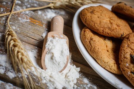 Oatmeal cakes with raisins, flour and spikelets of wheat on a wooden brown surfaceの写真素材
