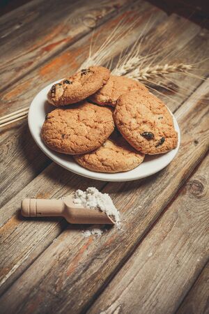 Oatmeal cakes with raisins, flour and spikelets of wheat on a wooden brown surfaceの写真素材