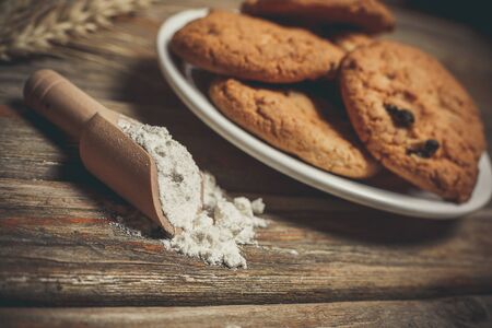 Oatmeal cakes with raisins, flour and spikelets of wheat on a wooden brown surfaceの写真素材