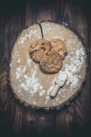 Oatmeal cakes with raisins, flour and spikelets of wheat on a wooden brown surfaceの写真素材