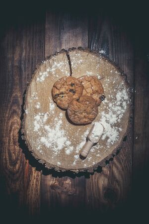Oatmeal cakes with raisins, flour and spikelets of wheat on a wooden brown surfaceの写真素材