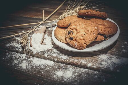 Oatmeal cakes with raisins, flour and spikelets of wheat on a wooden brown surfaceの写真素材