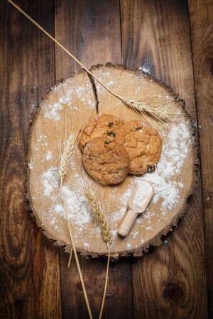 Oatmeal cakes with raisins, flour and spikelets of wheat on a wooden brown surfaceの写真素材