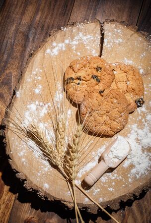 Oatmeal cakes with raisins, flour and spikelets of wheat on a wooden brown surfaceの写真素材