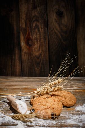 Oatmeal cakes with raisins, flour and spikelets of wheat on a wooden brown surfaceの写真素材