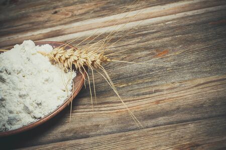 Flour and spikelets of wheat for baking bread lies on a wooden brown surfaceの写真素材
