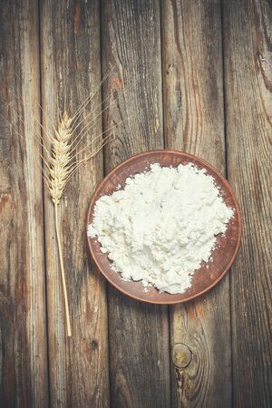Flour and spikelets of wheat for baking bread lies on a wooden brown surfaceの写真素材