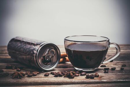 Coffee beans in a plastic jar and grains lie nearby on a wooden brown tableの写真素材