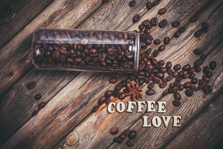 Coffee beans in a plastic jar and grains lie nearby on a wooden brown tableの写真素材