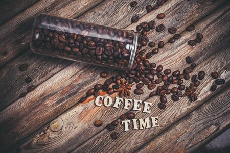 Coffee beans in a plastic jar and grains lie nearby on a wooden brown tableの写真素材