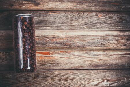 Coffee beans in a plastic jar and grains lie nearby on a wooden brown tableの写真素材