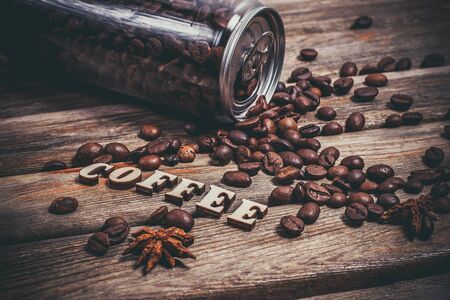 Coffee beans in a plastic jar and grains lie nearby on a wooden brown table