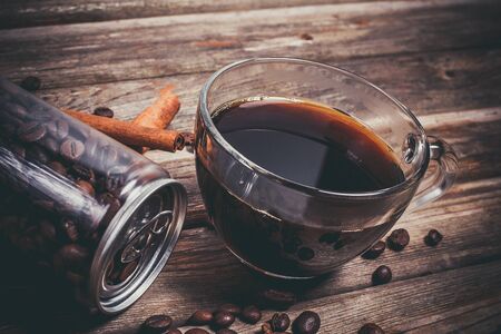 Coffee beans in a plastic jar and grains lie nearby on a wooden brown tableの写真素材