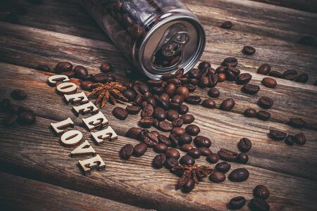 Coffee beans in a plastic jar and grains lie nearby on a wooden brown tableの写真素材