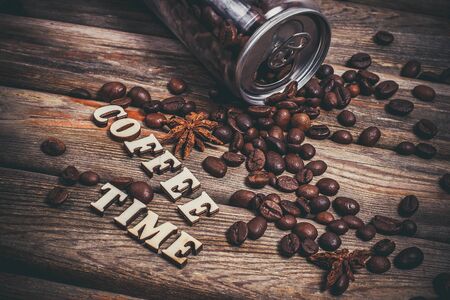 Coffee beans in a plastic jar and grains lie nearby on a wooden brown tableの写真素材