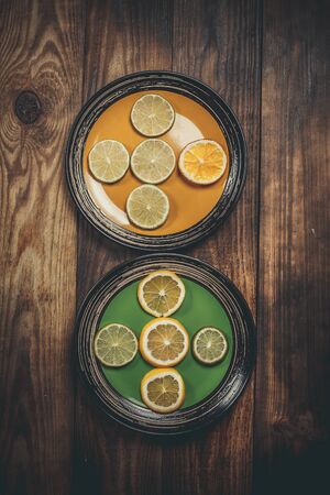 Lime and lemon citruses on beautiful colored plates on a wooden tableの写真素材