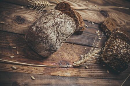 Fragrant black bread with spices, grains and ears of wheat on a wooden vintage surface