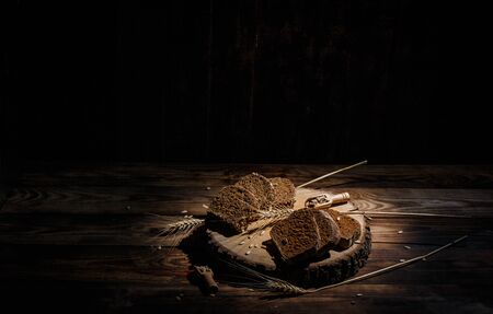 Fragrant black bread with spices, grains and ears of wheat on a wooden vintage surfaceの写真素材