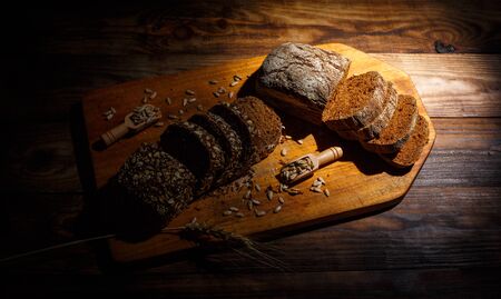 Fragrant black bread with spices, grains and ears of wheat on a wooden vintage surfaceの写真素材