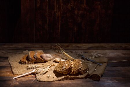 Fragrant black bread with spices, grains and ears of wheat on a wooden vintage surfaceの写真素材