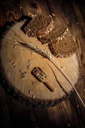 Fragrant black bread with spices, grains and ears of wheat on a wooden vintage surface