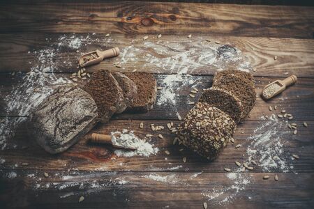 Fragrant black bread with spices, grains and ears of wheat on a wooden vintage surface