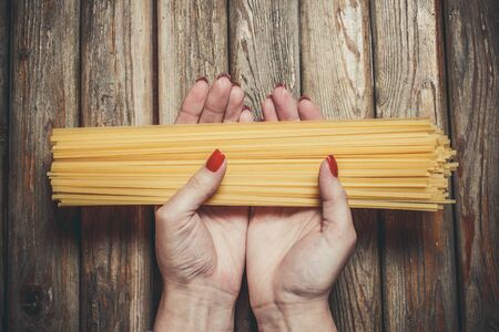Raw pasta in the hands of a girl for cooking pasta on a wooden backgroundの写真素材