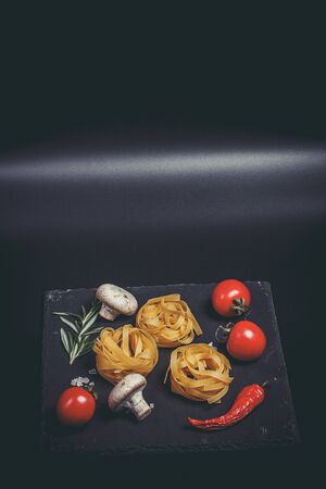 Raw pasta with vegetables, and spices on a black surfaceの写真素材