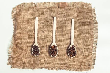 Fragrant coffee grains in light wooden spoons on a white backgroundの写真素材