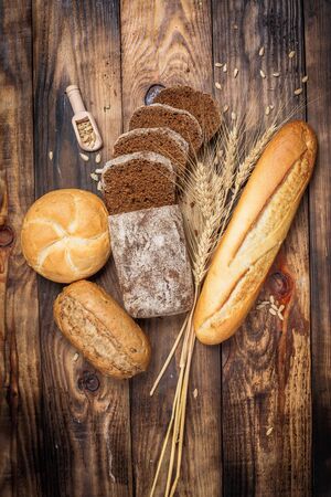Different buns of fresh bread and spikelets of wheat on a vintage backgroundの写真素材