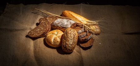Different buns of fresh bread and spikelets of wheat on a vintage backgroundの写真素材