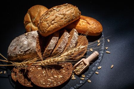 Different buns of fresh bread and spikelets of wheat on a black backgroundの写真素材
