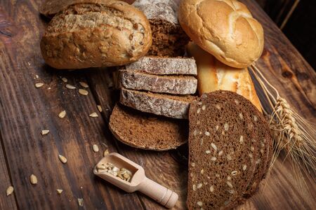 Different buns of fresh bread and spikelets of wheat on a vintage background