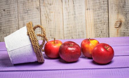 Beautiful red sweet apples on a purple background and in a white bucketの写真素材