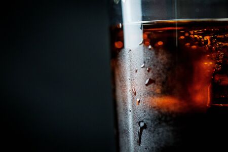 Soda in a glass on a black background with ice cubes and drops closeの写真素材
