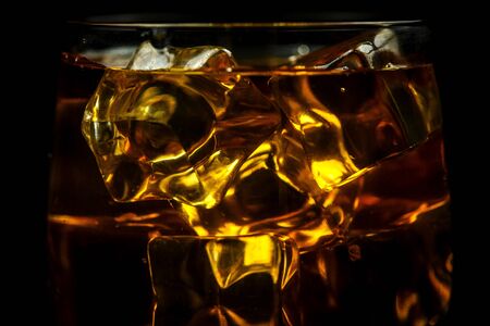 Glass with whiskey and ice cubes on a black background closeの写真素材