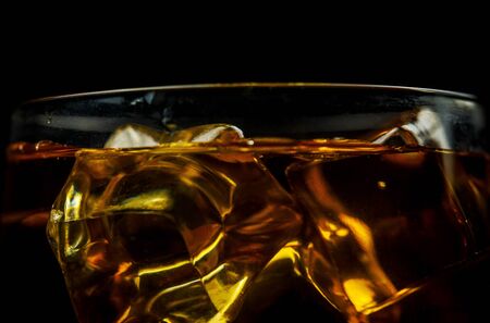 Glass with whiskey and ice cubes on a black background closeの写真素材