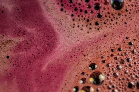 Pink foam of a delicious drink near the glass is very close