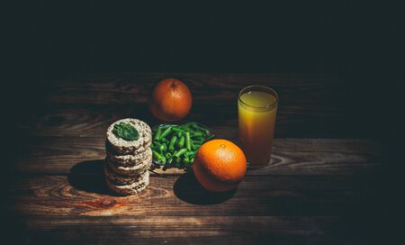 Glass of orange juice and orange, bread rolls and green beans for diet near on a wooden tableの写真素材