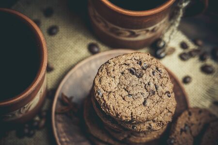 Brown clay vintage coffee mugs and delicious chocolate chip cookies on a wooden table in warm colorsの写真素材
